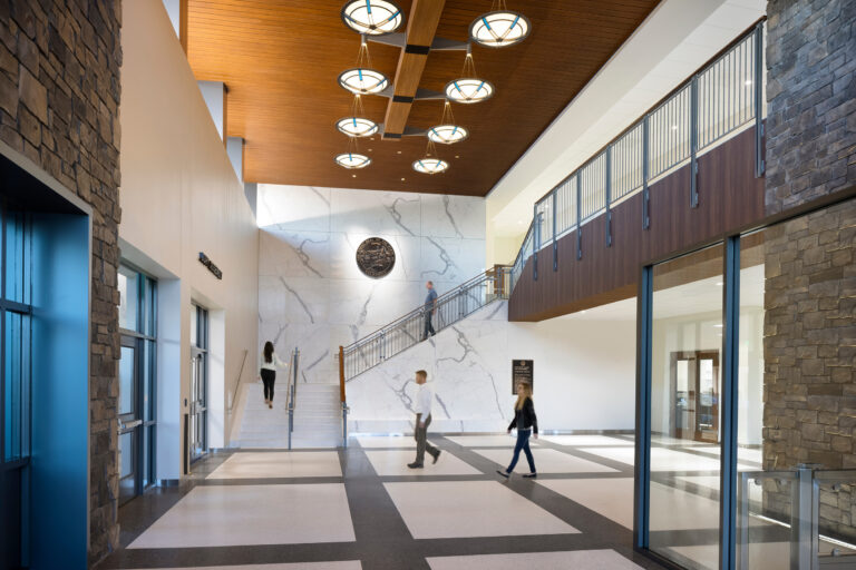 Spacious modern courthouse lobby with stone walls, a marble stairway, wood ceiling, and people walking through.