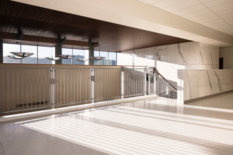 Sunlit courthouse interior with metal railings, marble walls, pendant lights, and a sign reading Jury Assembly
