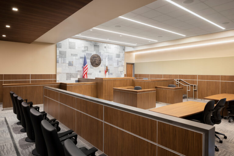 Modern courtroom interior with wood paneling, judge’s bench, jury box, and U.S. and California flags beneath the state seal