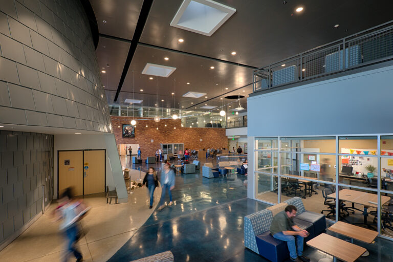 Modern building atrium with glass meeting rooms, lounge seating, and people walking across a polished floor