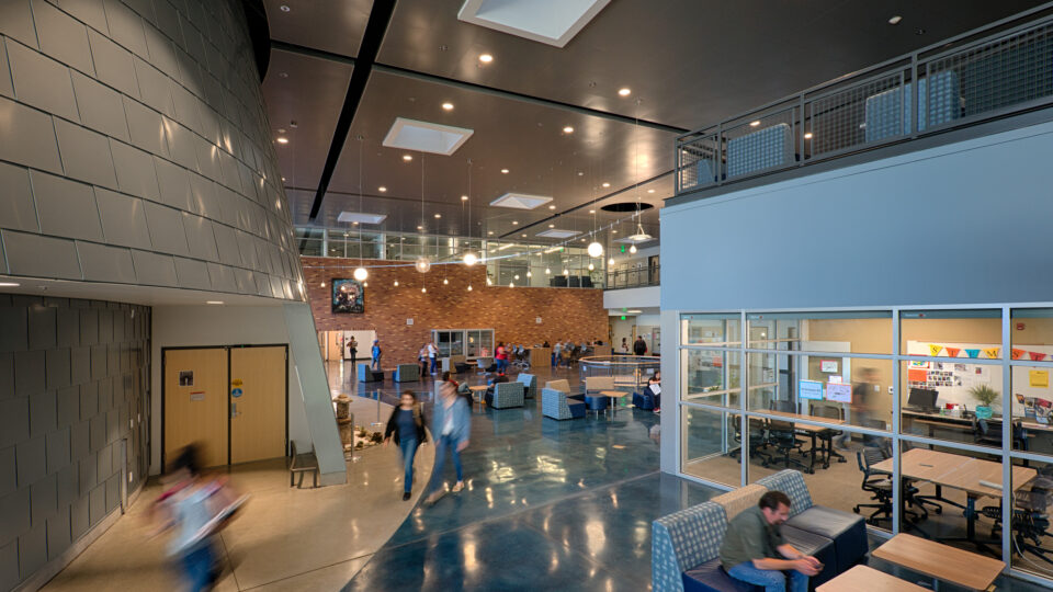 Modern building atrium with glass meeting rooms, lounge seating, and people walking across a polished floor