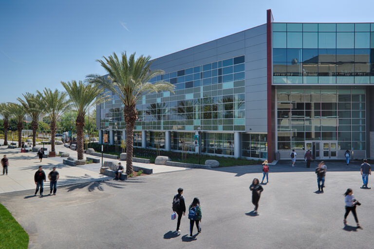 Modern glass-fronted campus building with palm trees and students walking outside on a sunny day