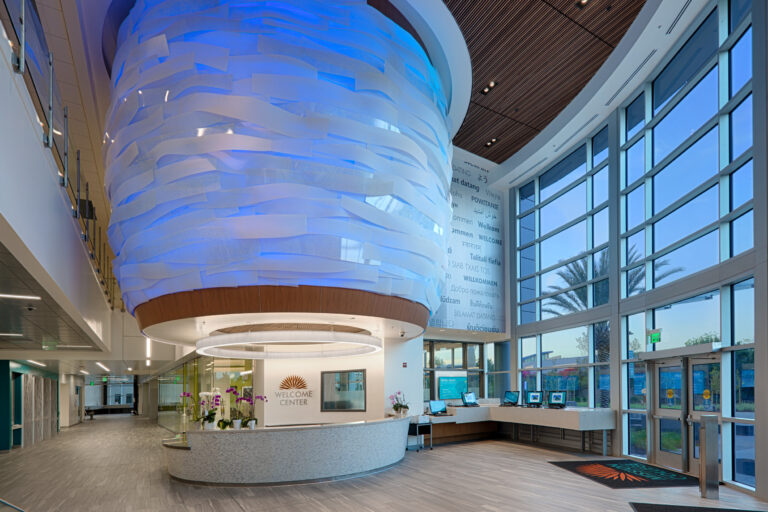 Modern welcome center lobby with a curved reception desk and large blue-lit hanging sculpture by tall windows
