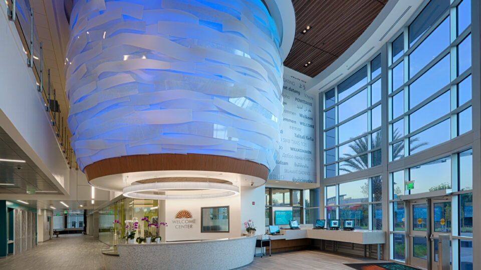 Modern welcome center lobby with a curved reception desk and large blue-lit hanging sculpture by tall windows