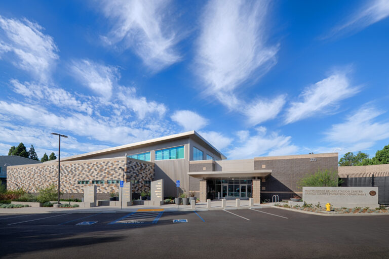Modern rehabilitation center building with accessible parking, under a bright blue sky with wispy clouds.