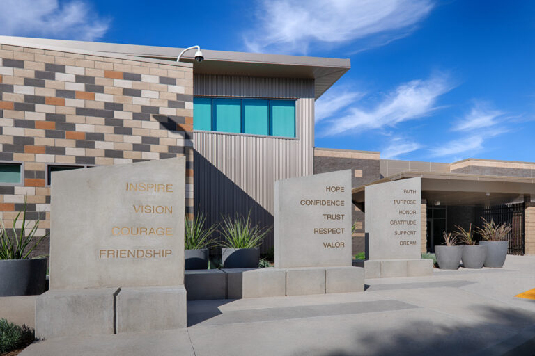 Modern building entrance with concrete pillars engraved with words like Inspire, Vision, Courage, Hope, and Trust.