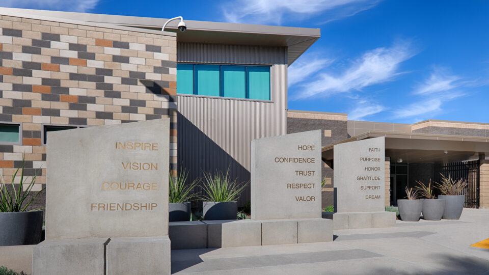 Modern building entrance with concrete pillars engraved with words like Inspire, Vision, Courage, Hope, and Trust.