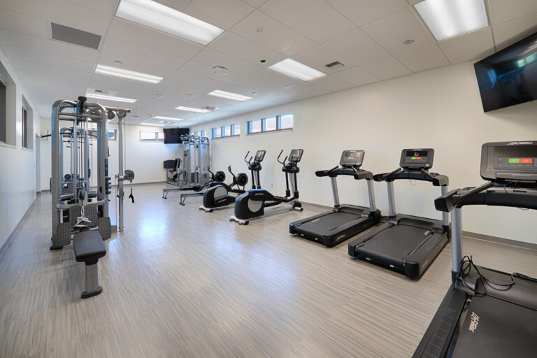 Bright modern fitness room with treadmills, ellipticals, rowing machines, and a cable weight machine.