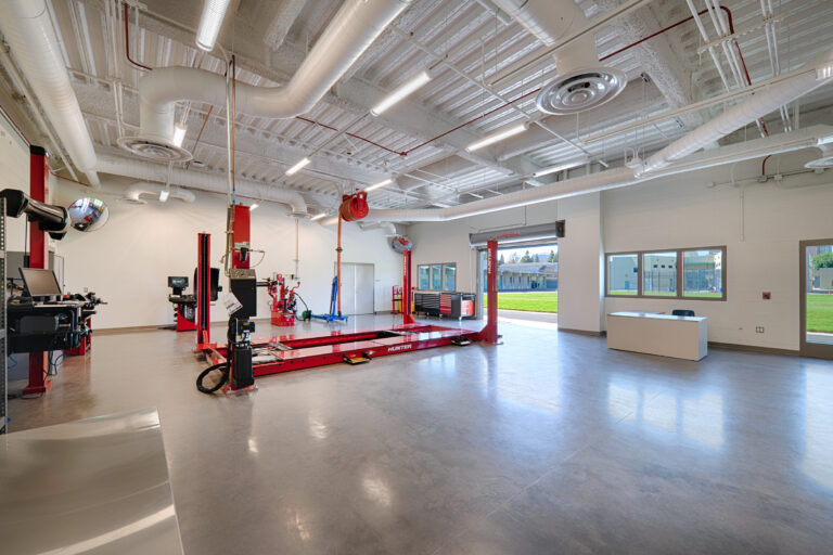 Bright automotive workshop with red vehicle lift, tire service machines, polished concrete floor, and large open bay door