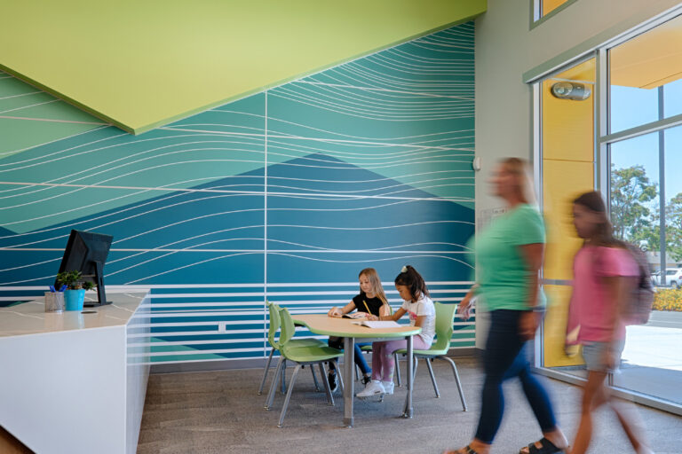Bright modern lobby with a blue-green mural, two children seated at a table, and blurred people walking by glass doors