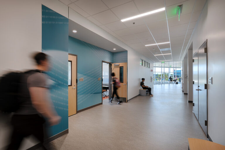 Bright modern hallway with classrooms, students walking and sitting, and blue walls patterned with binary code