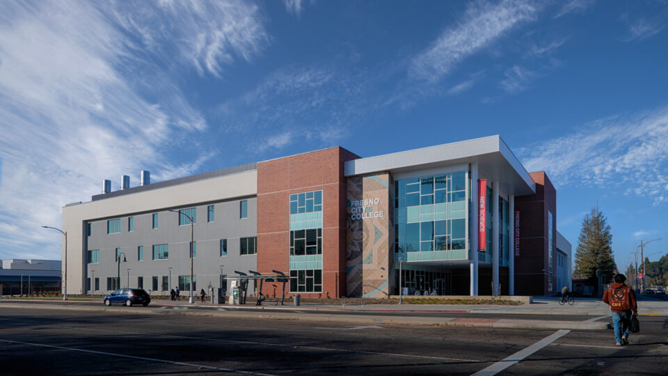 Fresno City College science building at a street corner, with brick and glass facade under a bright blue sky.