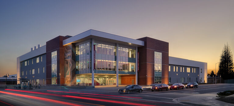 Fresno City College Science building at dusk, with a glass-front entrance and red light trails from passing cars