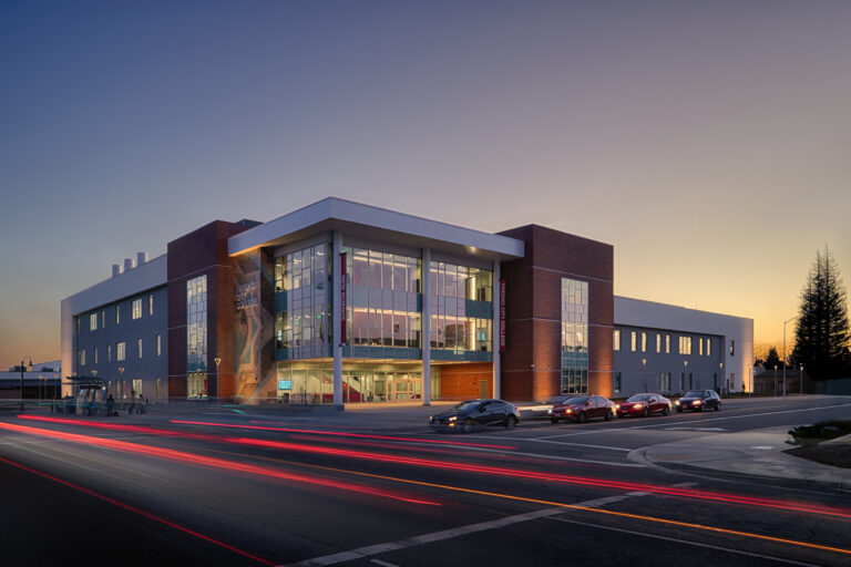 Fresno City College Science building at dusk, with a glass-front entrance and red light trails from passing cars