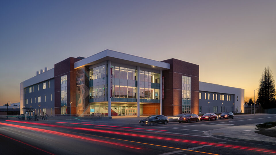 Fresno City College Science building at dusk, with a glass-front entrance and red light trails from passing cars