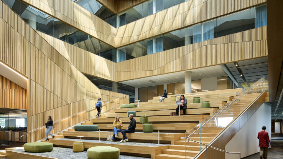 Modern wood-paneled atrium with tiered seating, skylights, and people studying and talking on the steps