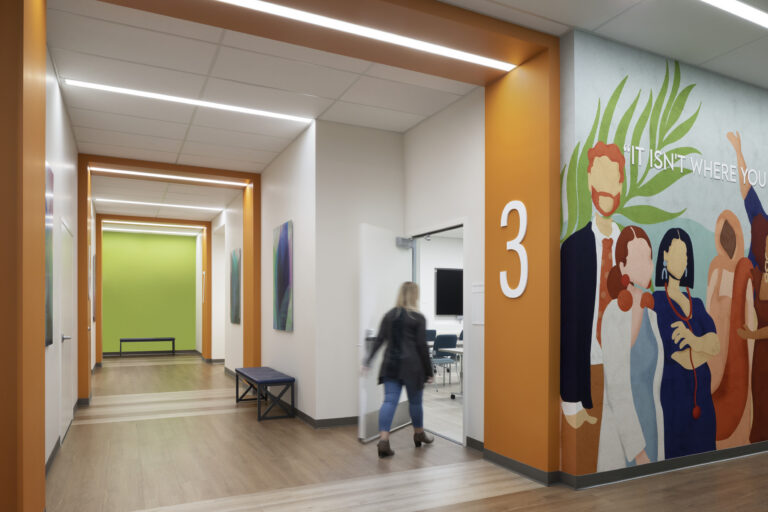 Bright modern hallway with orange accents, a large 3, colorful mural, and a person entering a room.