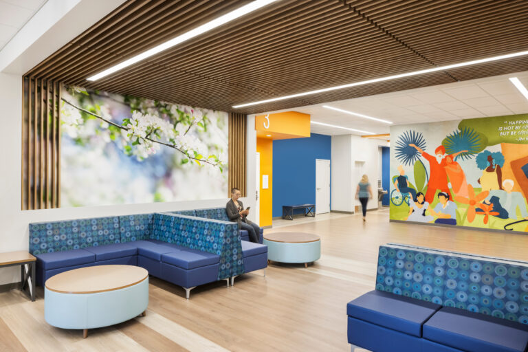 Modern waiting area with blue booth seating, wood-slat ceiling, floral wall art, and a colorful mural on the right.