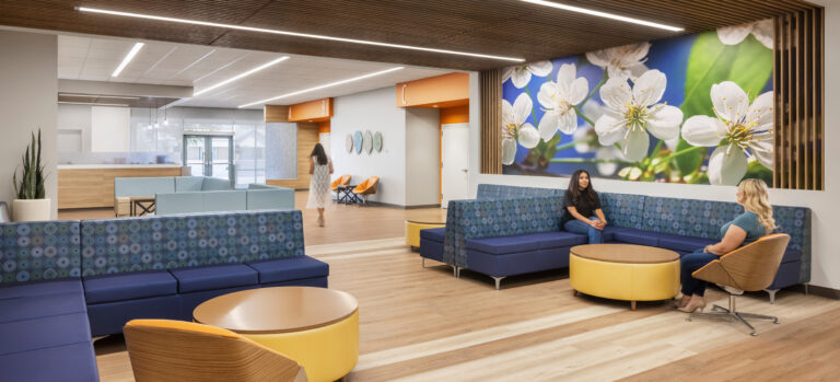 Modern medical office waiting area with blue seating, wood accents, and a large floral wall mural.