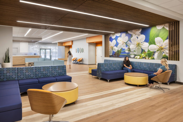 Modern medical office waiting area with blue seating, wood accents, and a large floral wall mural.