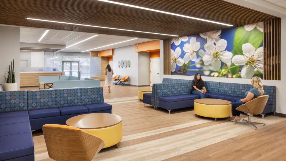 Modern medical office waiting area with blue seating, wood accents, and a large floral wall mural.