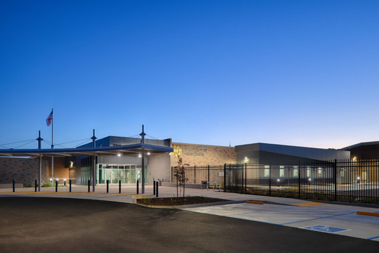 Department of Corrections building entrance at dusk, with a fenced perimeter, flagpole, and empty parking area