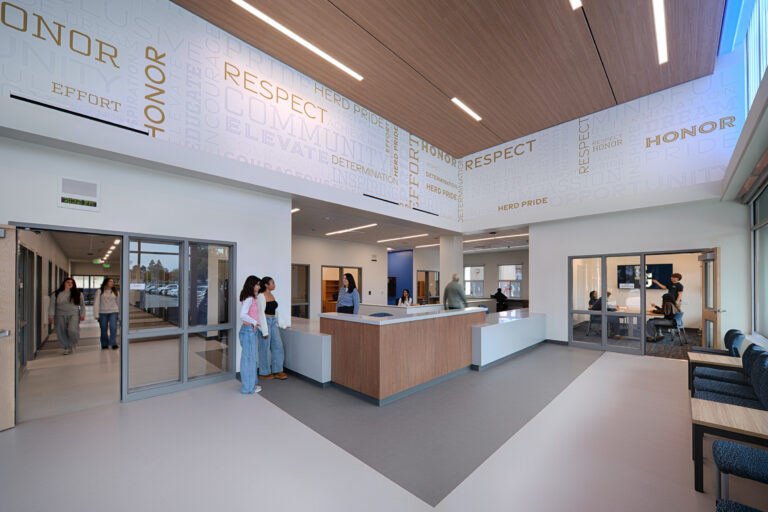 Modern school lobby with reception desk, students and staff, and large wall graphics reading Honor, Respect, and Effort