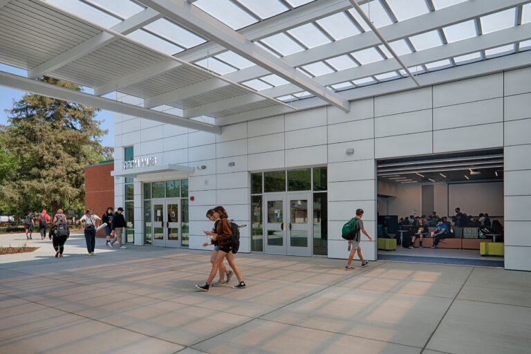 Students walk past the Tech Hub entrance beneath a large covered canopy, with more students gathered inside.