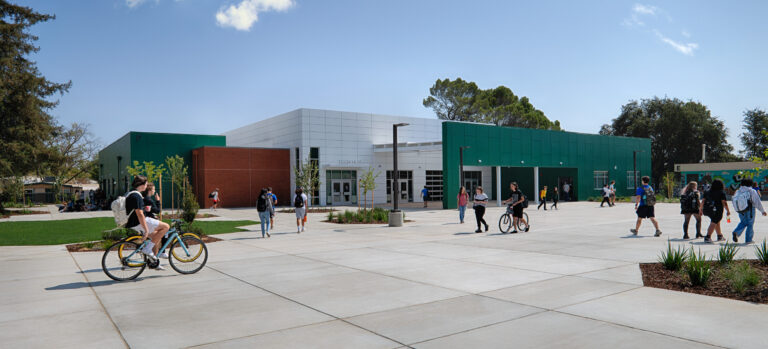 Students walk and ride bikes across a courtyard outside a modern green-and-white school building labeled Tech Hub.