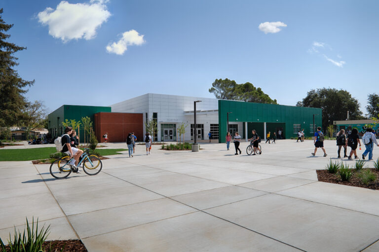 Students walk and ride bikes across a courtyard outside a modern green-and-white school building labeled Tech Hub.