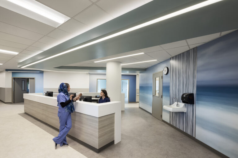 Modern hospital nurses’ station with two staff members, blue ocean-themed walls, and bright linear ceiling lights
