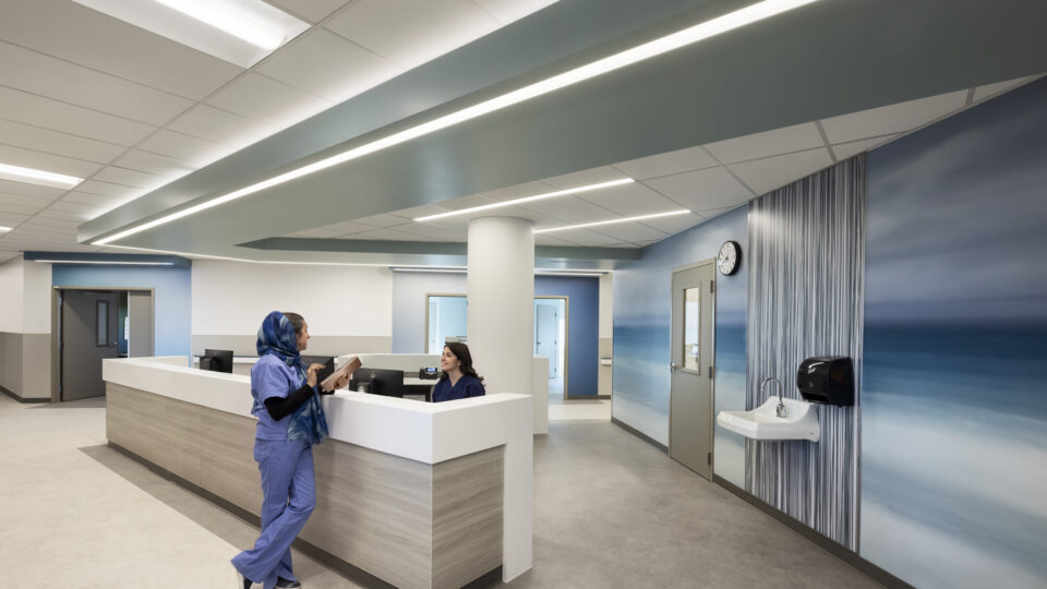 Modern hospital nurses’ station with two staff members, blue ocean-themed walls, and bright linear ceiling lights