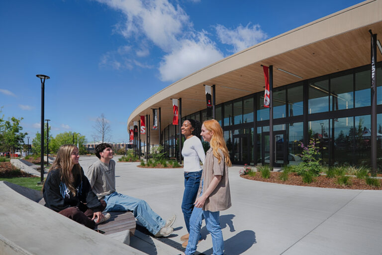 Four students talking outside a modern campus building with Sierra College and Wolverines banners on a sunny day