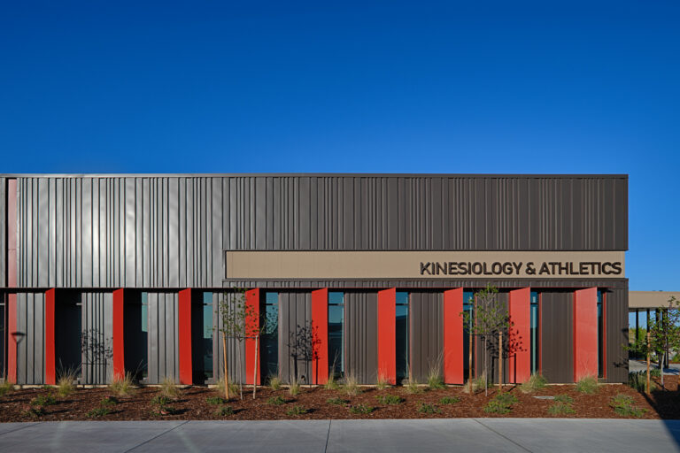 Modern building with red vertical accents and a sign reading Kinesiology & Athletics under a clear blue sky