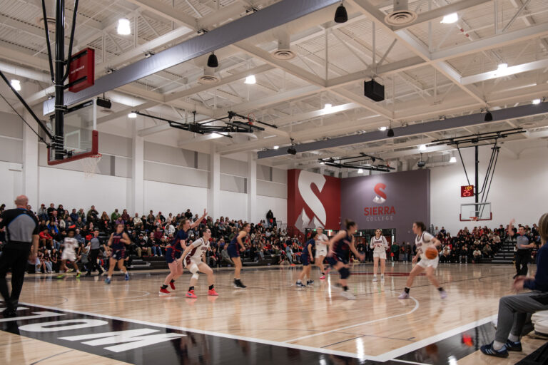 Women’s basketball game in a packed Sierra College gym, with players in motion on the court and spectators watching.