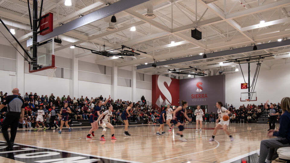 Women’s basketball game in a packed Sierra College gym, with players in motion on the court and spectators watching.