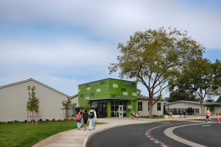 Students walking toward the green McManus Administration building on a school campus.