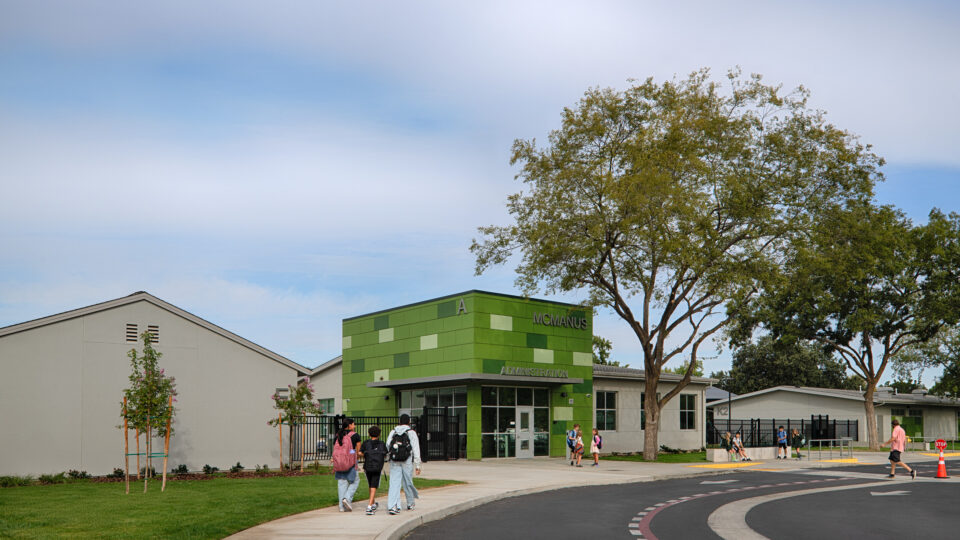 Students walking toward the green McManus Administration building on a school campus.