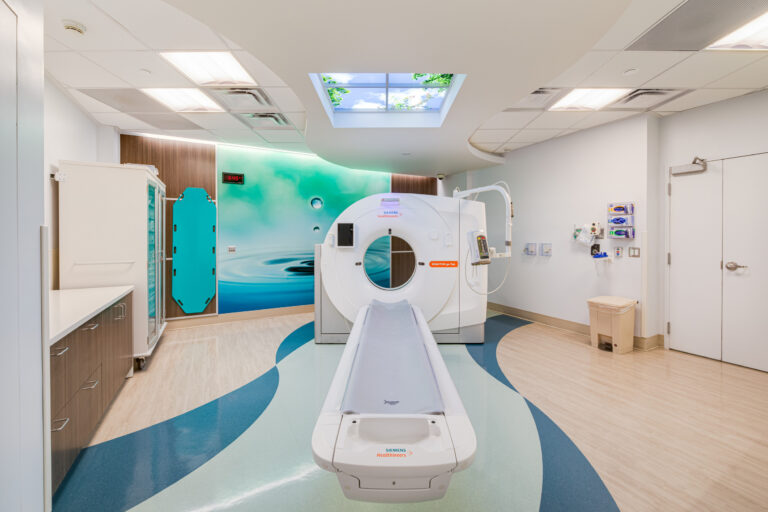 Modern hospital CT scan room with scanner bed, blue wave-pattern floor, and calming water mural on the wall