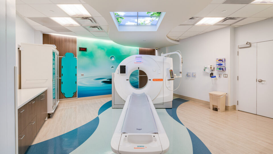Modern hospital CT scan room with scanner bed, blue wave-pattern floor, and calming water mural on the wall