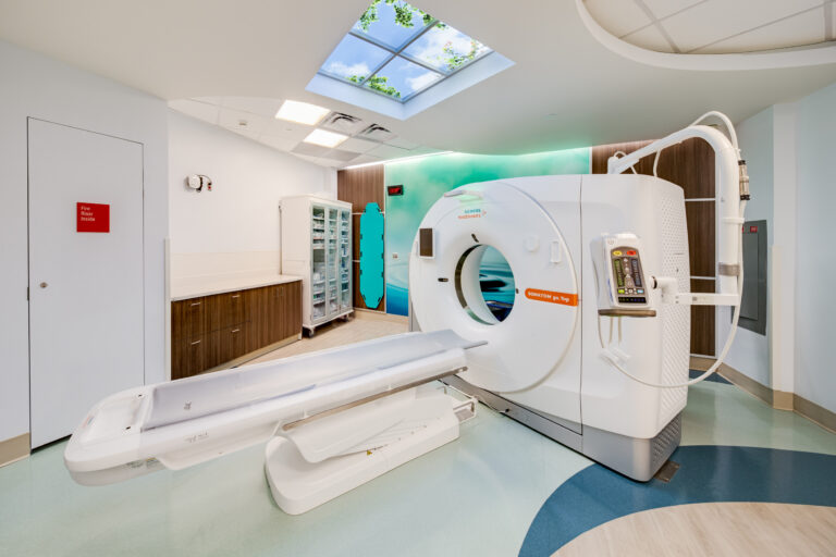 Modern hospital CT scan room with scanner bed, wood cabinets, and a skylight ceiling showing blue sky and leaves