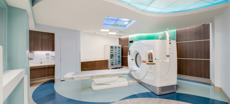 Modern hospital CT scan room with a white scanner, wood cabinets, and blue ambient ceiling lighting