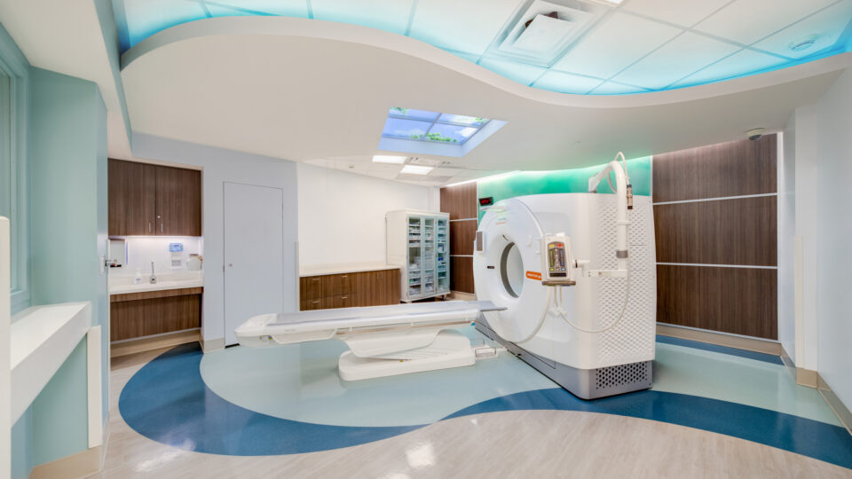 Modern hospital CT scan room with a white scanner, wood cabinets, and blue ambient ceiling lighting