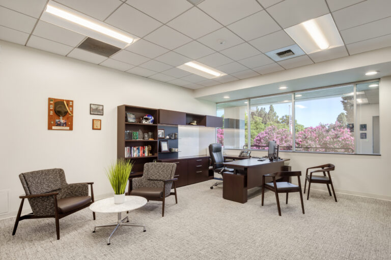 Modern private office with desk, guest chairs, bookshelf, and large windows overlooking pink flowering trees