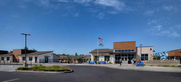 Front entrance of Katherine Johnson Middle School with students outside, flags flying, and a wide blue sky.