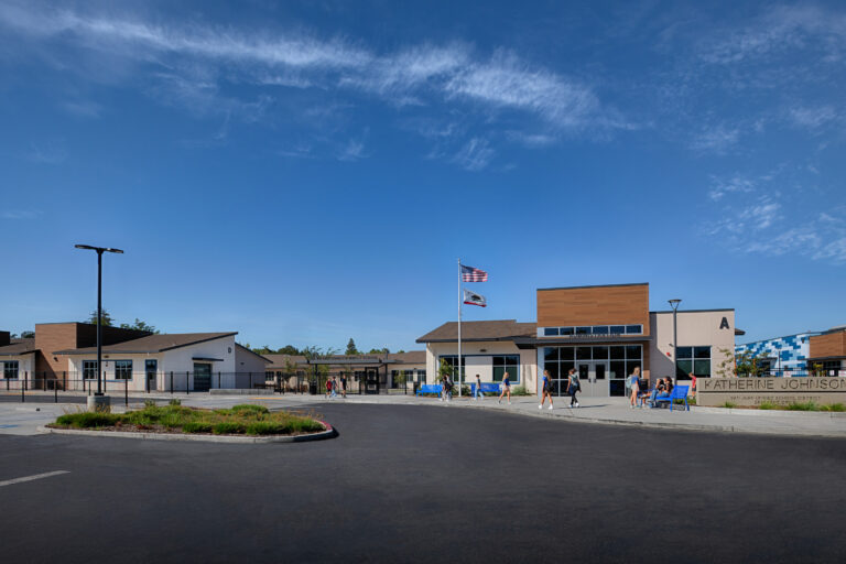 Front entrance of Katherine Johnson Middle School with students outside, flags flying, and a wide blue sky.