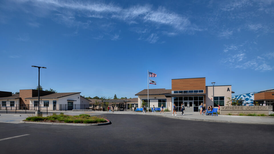 Front entrance of Katherine Johnson Middle School with students outside, flags flying, and a wide blue sky.