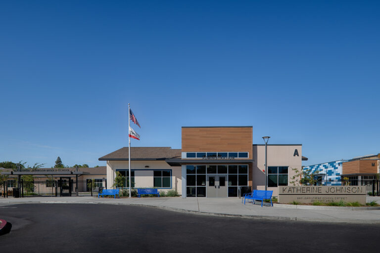 Front entrance of Katherine Johnson Middle School administration building with flags, blue benches, and clear sky