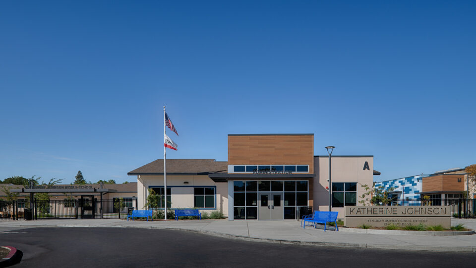 Front entrance of Katherine Johnson Middle School administration building with flags, blue benches, and clear sky