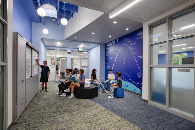 Students collaborating in a modern school hallway with whiteboard cabinets and a blue Freedom 7 wall mural.